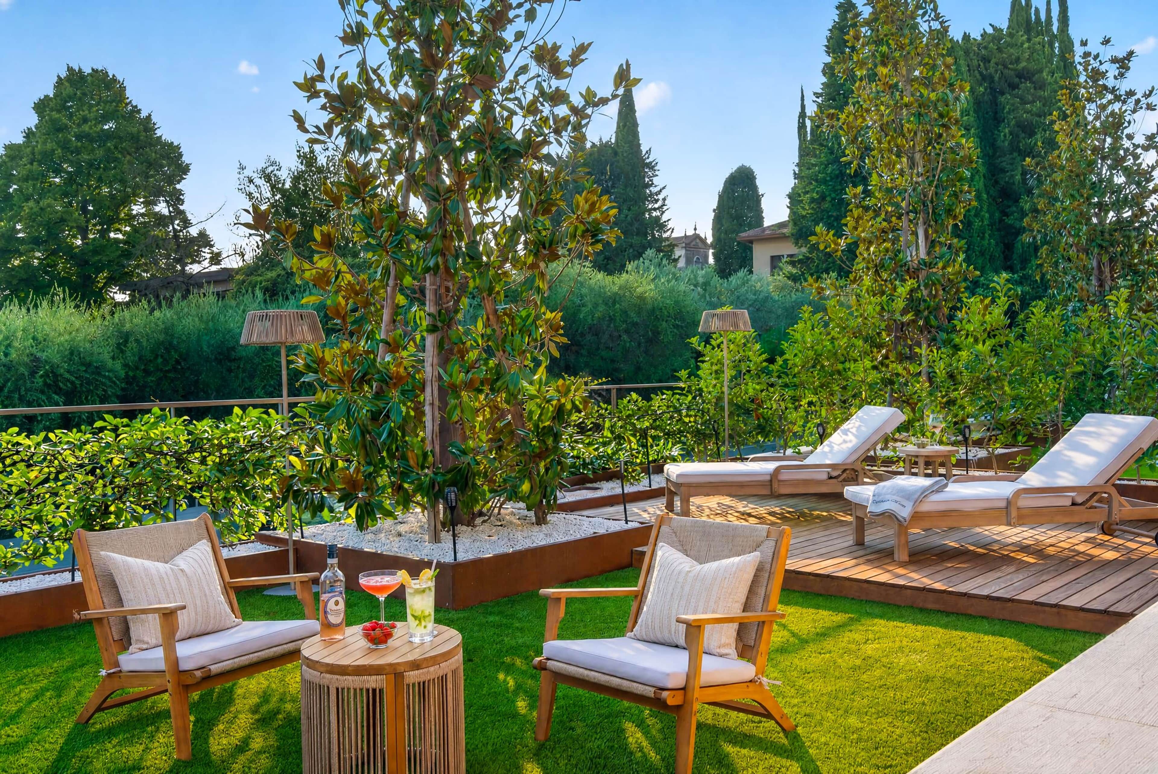 Eine Terrassenfläche mit Sitzgelegenheiten im Freien, einem kleinen Tisch mit einem Getränk und einem Zierbaum.
