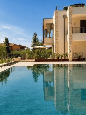 A clear swimming pool with a stone facade building in the background. - NEW: Casa Serenia - Residence Corte Carden 2 (Bardolino)