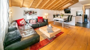 A modern living room with a leather sofa, a wooden coffee table, and a dining area with a TV. - Victoria C - InspiringPlaces (Zermatt)