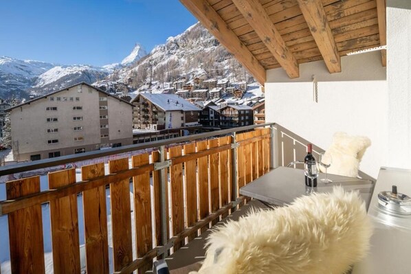 A balcony with a wooden railing overlooking a mountainous village with snow-covered buildings. - Victoria C - InspiringPlaces (Zermatt)