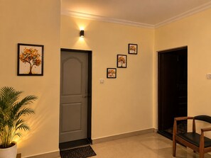 A hallway with a door, a wall-mounted light, and a potted plant. - Storio Hotel & Resort (Panaji)