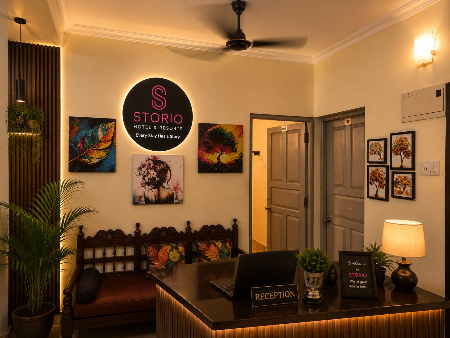 Zona de recepción de un hotel con mostrador, ventilador de techo y obras de arte colgadas en la pared.