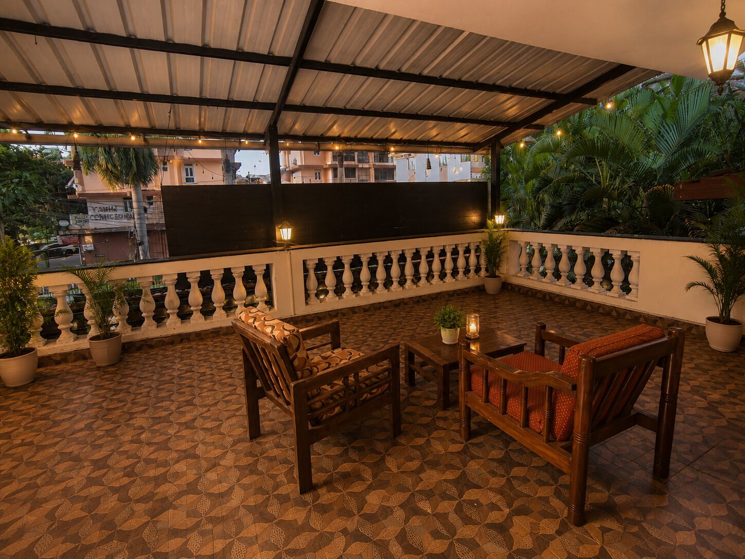 An outdoor seating area with patterned flooring, wooden furniture, potted plants, and a view of the cityscape.