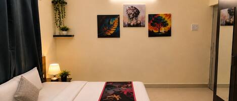 Una habitación de hotel con cama, mesita de noche con lámpara, aire acondicionado instalado en la pared y una obra de arte en la pared.