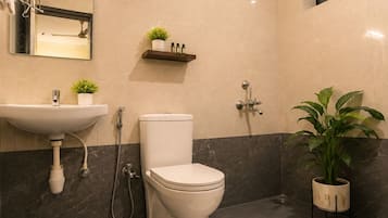Un baño moderno con inodoro, lavamanos y ducha. Hay un espejo sobre el lavamanos, un estante con artículos de aseo y una planta en maceta.