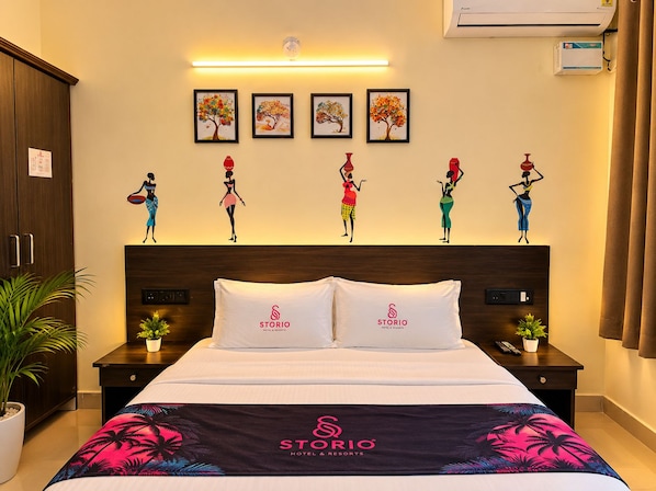 A hotel room with a bed, two nightstands, a wall-mounted air conditioner, and a series of framed artworks above the bed.