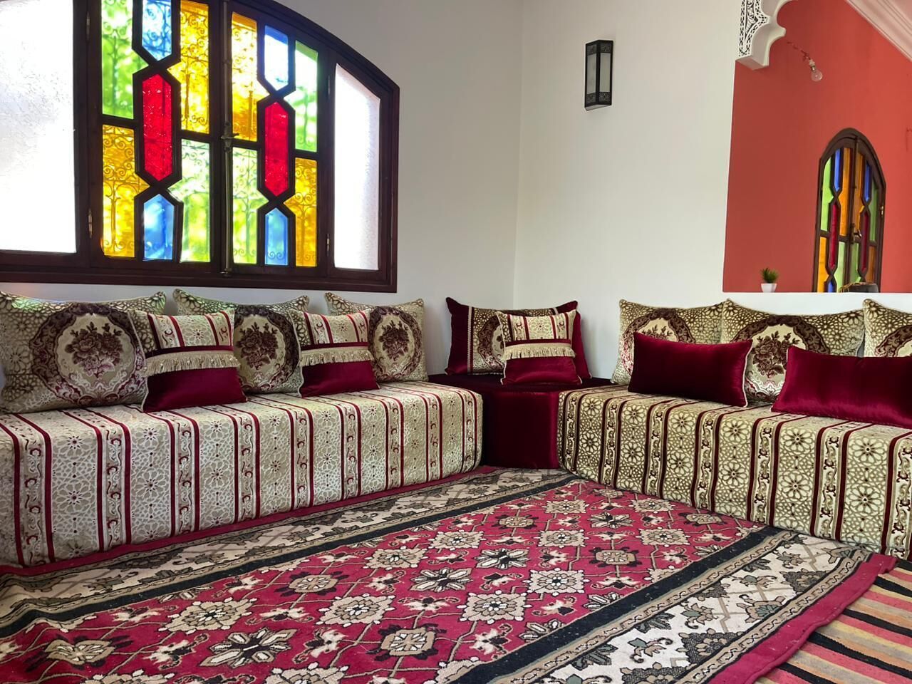 Une pièce avec un canapé placé contre un mur, un tapis à motifs et une fenêtre à vitraux.