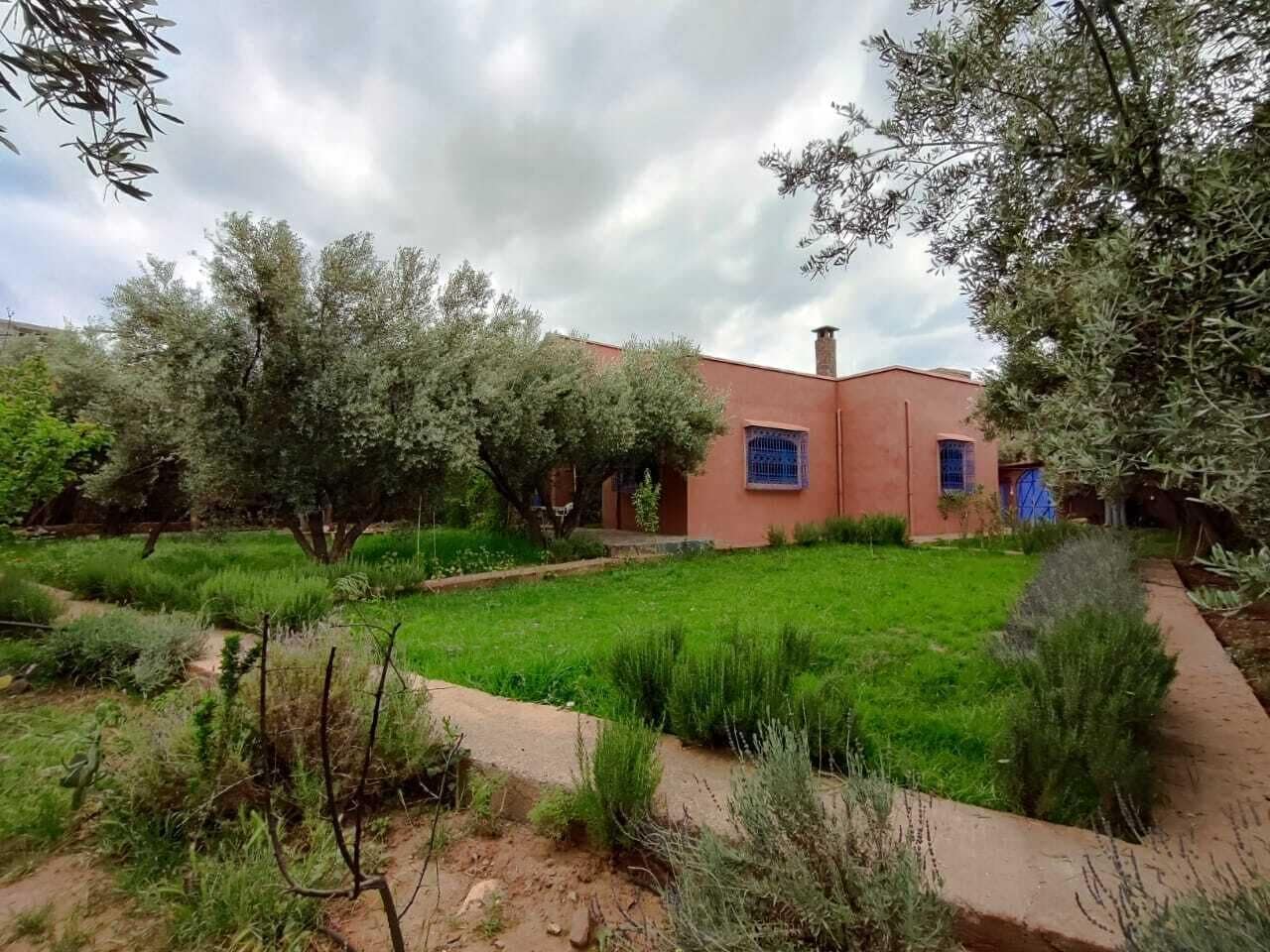 Un bâtiment à l’extérieur rouge, entouré d’une zone verdoyante avec des arbres et des arbustes.