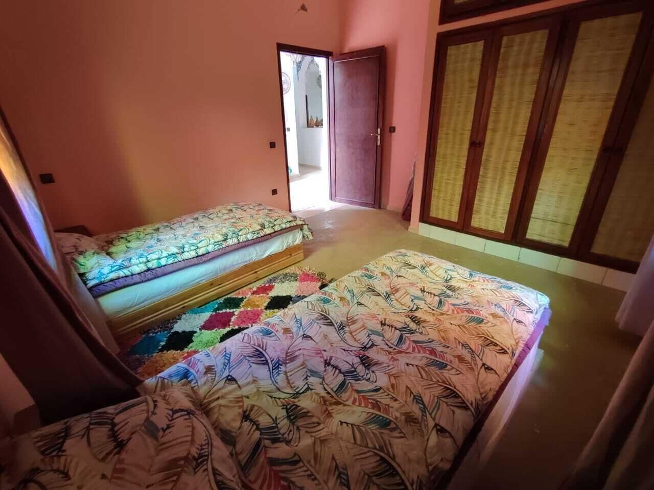 A room with two beds, a colorful rug, and a wooden door.
