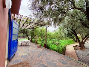 En udendørs patio med flisebelagte gulve, en pergola og et bord med stole.