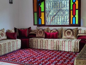 A room with a sofa set against a wall, a patterned rug, and a window with decorative glass. - Villa Tissi house (Marrakech)
