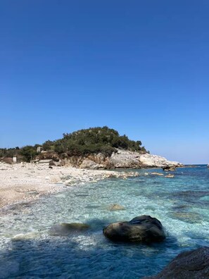 A beach with clear water, rocks, and a hill with trees.