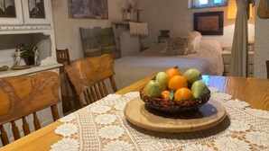 A dining area with a table set for two, featuring a fruit bowl and a lace tablecloth.