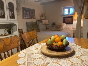 A dining area with a table set for two, featuring a fruit bowl and a lace tablecloth.