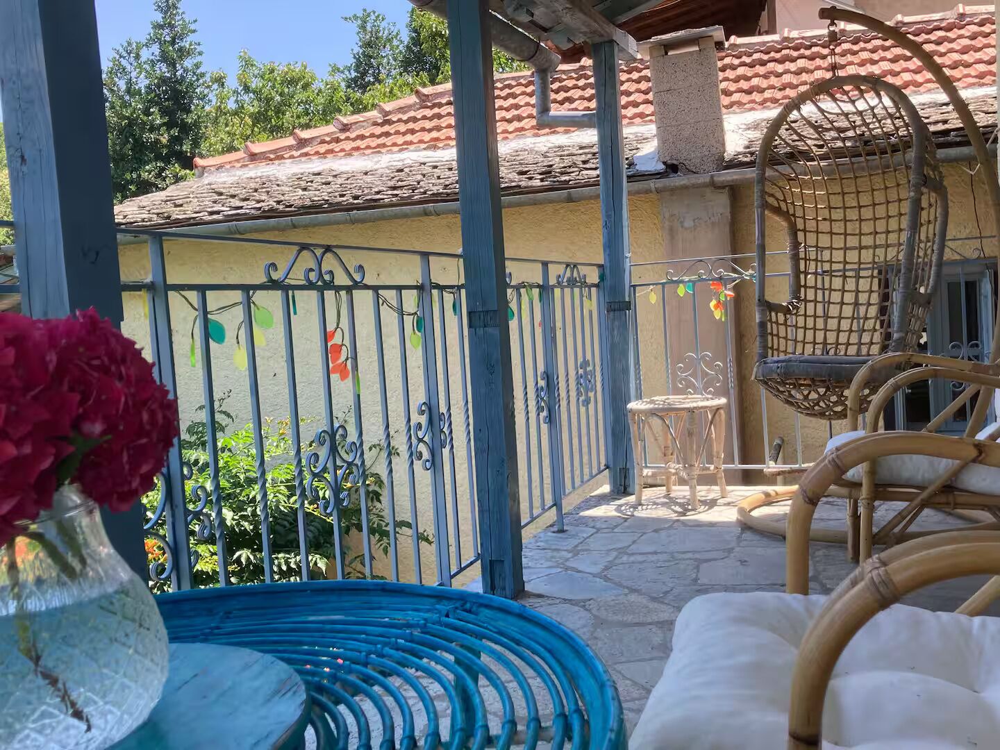 A covered outdoor area with a metal fence, wicker furniture, and a potted plant.