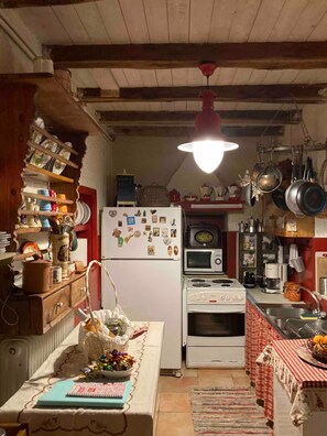 A kitchen with a white stove, a microwave, and a refrigerator. There are shelves with dishes and a basket on the table. - Valley Cottage: Traditional 2-bedroom House (Tsagkarada)