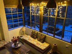 Una habitación acogedora con un banco, una mesa con un florero y una ventana con luces colgantes.