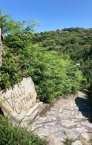 Un escalier en pierre mène à une pancarte indiquant « Valley Cottage », au milieu d’une végétation luxuriante.