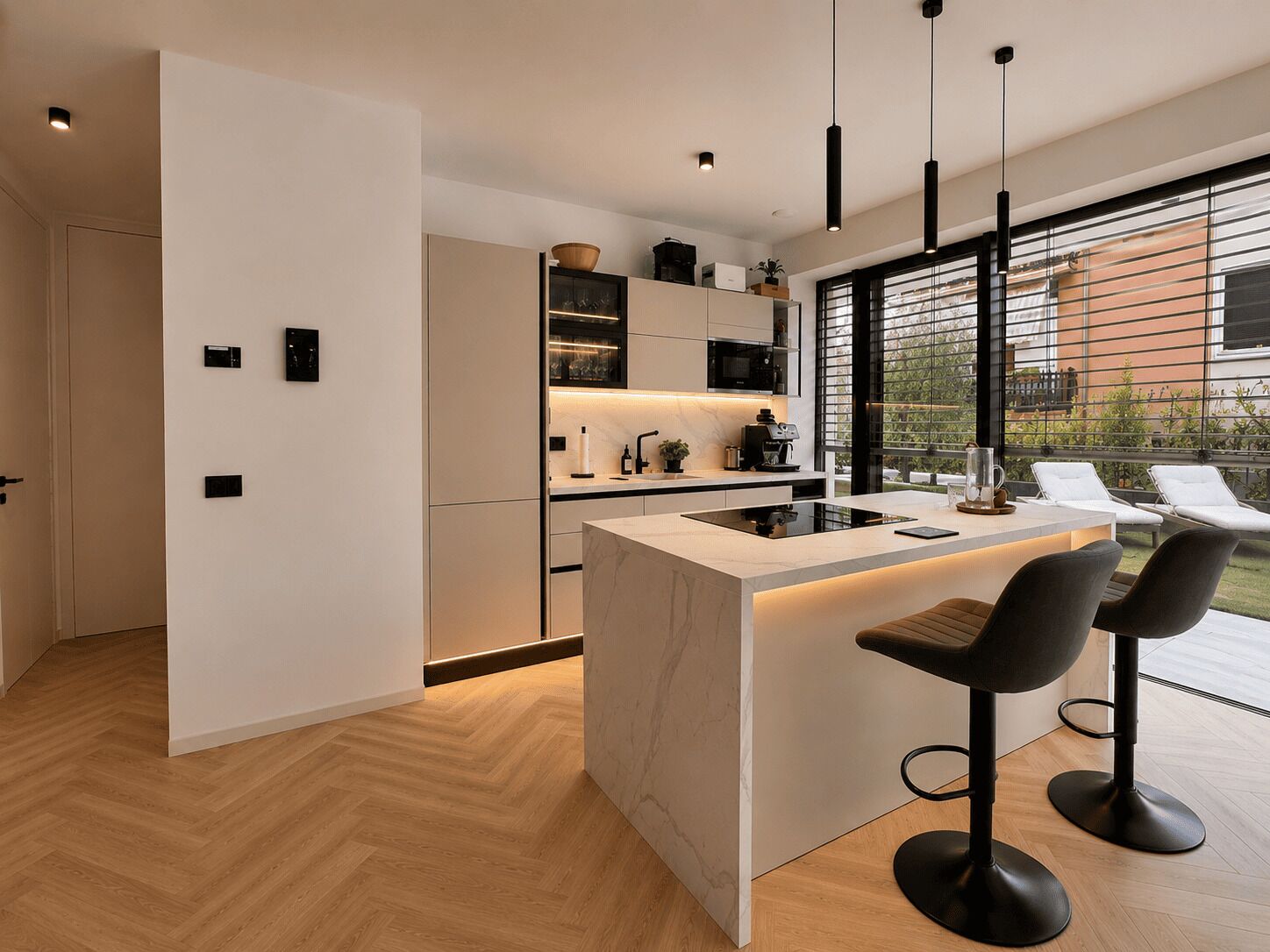 Une cuisine moderne dotée d’un îlot central, de tabourets de bar noirs et offrant une vue sur l’extérieur grâce à de grandes fenêtres.