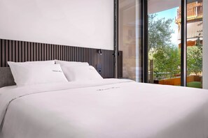 Ein modernes Hotelzimmer mit einem großen Bett, einem Holz-Kopfteil und Blick auf die Stadt durch raumhohe Fenster.