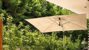 Une terrasse extérieure avec une table et des chaises en bois, un grand parasol et une végétation luxuriante en arrière-plan.