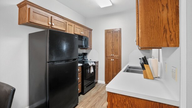 A compact kitchen with wooden cabinets, a black refrigerator, a microwave, and an oven. - Comfortable Living in Saddlebrook (Lumberton)