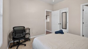 A bedroom with a bed, a desk with a chair, a ceiling fan, and a door leading to another room. - Comfortable Living in Saddlebrook (Lumberton)