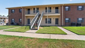 A multi-story apartment building with a central staircase, individual door numbers, and a parking area. - Comfortable Living in Saddlebrook (Lumberton)