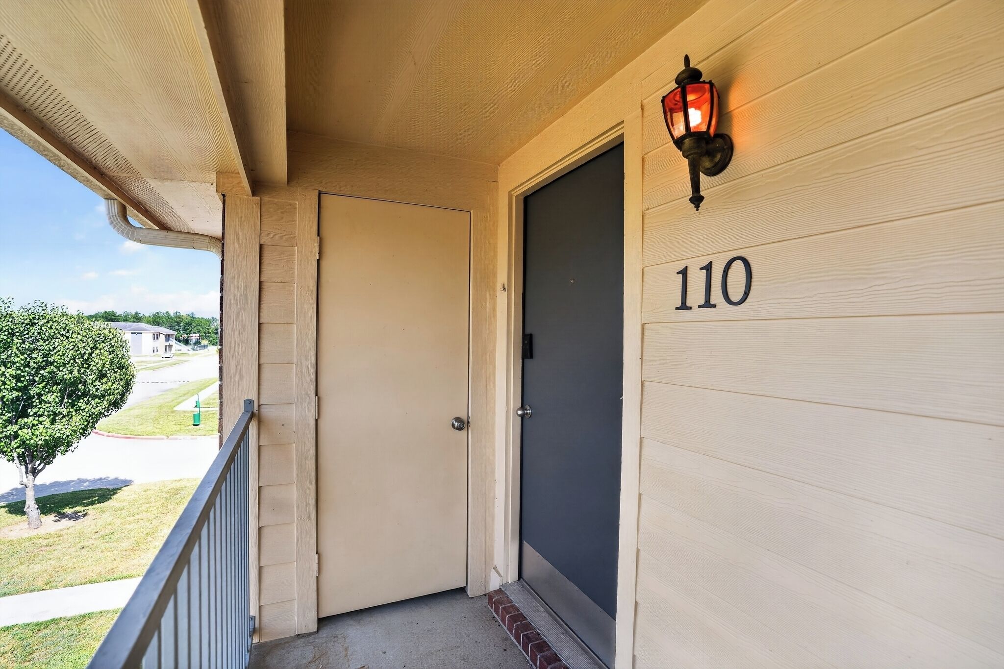A wooden door with the number 110, a small porch with a railing, and a wall-mounted light fixture.