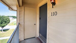 A wooden door with the number 110, a small porch with a railing, and a wall-mounted light fixture. - Comfortable Living in Saddlebrook (Lumberton)