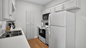 A modern kitchen with white cabinetry, a stainless steel sink, a microwave, a stove, and a refrigerator. - Saddlebrook: Comfortable Furnished Apartment (Lumberton)
