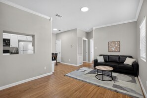 A modern living room with a black leather sofa, a round coffee table, and a gray rug. - Saddlebrook: Comfortable Furnished Apartment (Lumberton)