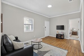 Un salon moderne avec un canapé en cuir noir, une table basse ronde et un téléviseur à écran plat fixé au mur.