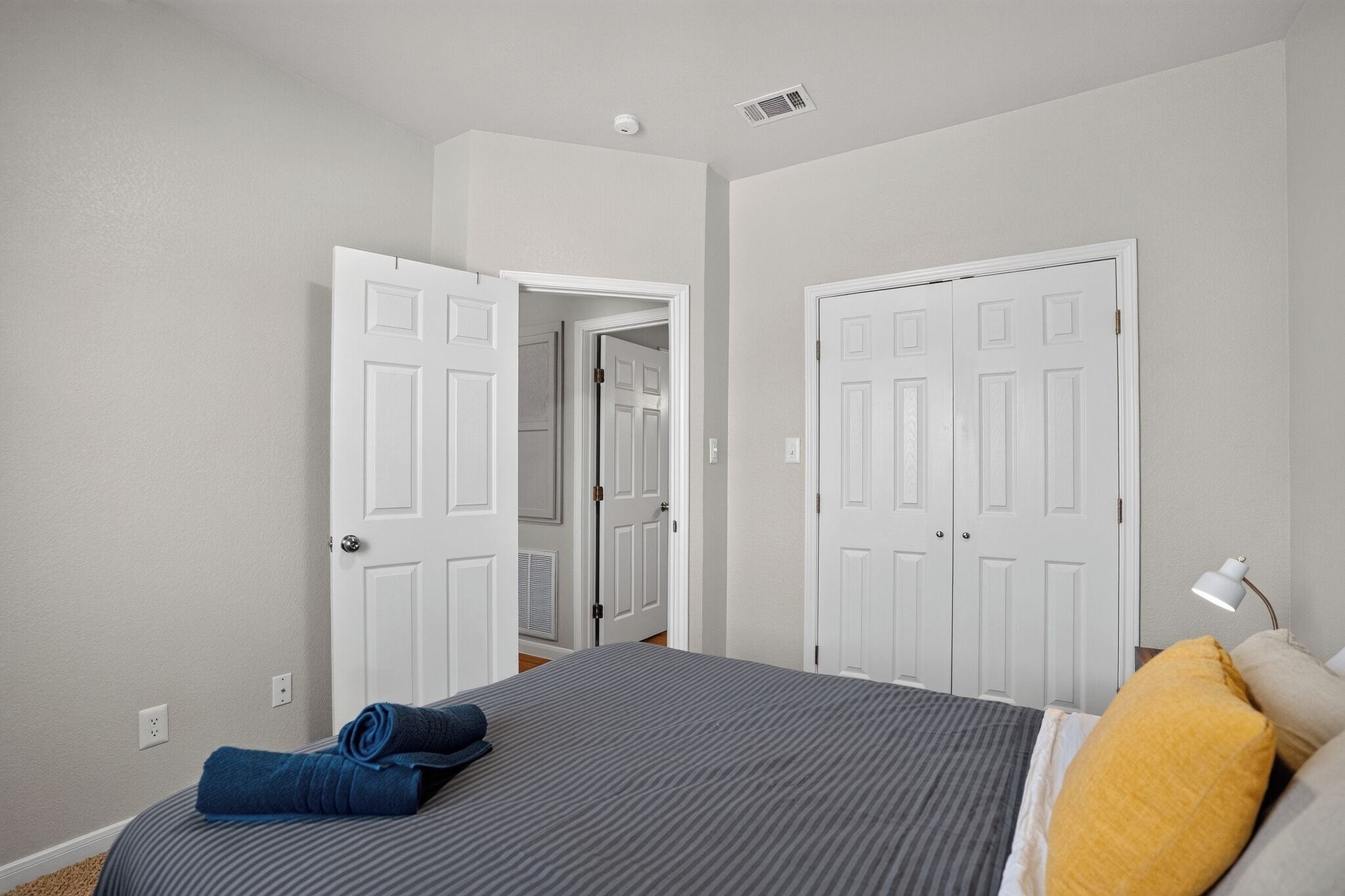 Un dormitorio con una cama, dos puertas, una lámpara y una ventana.