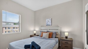 A bedroom with a bed, two bedside tables, a window, and a wall-mounted artwork. - Relax and Feel at Home at Saddlebrook (Lumberton)