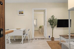 Een moderne woonkamer met een witte bank, een eettafel met stoelen, een wandgemonteerde flatscreen televisie en een potplant.