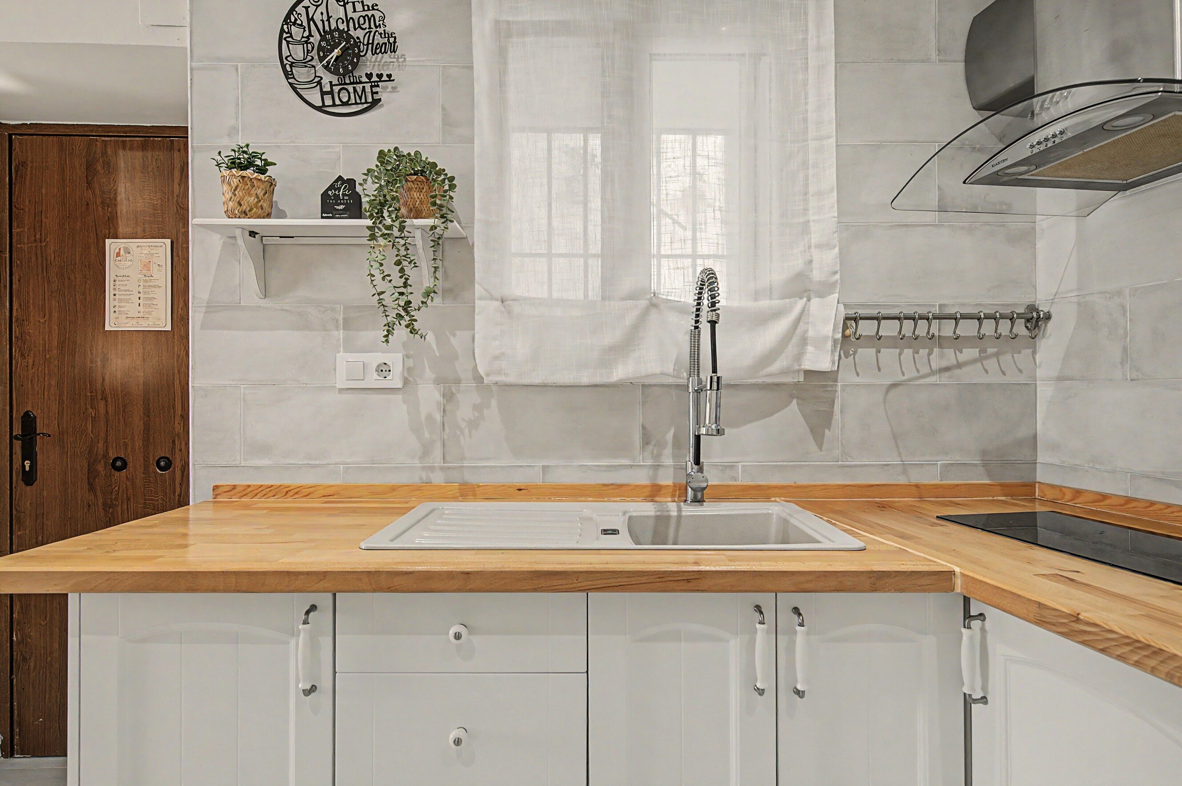 Een keuken met een houten aanrecht, een roestvrijstalen spoelbak en witte kastjes.