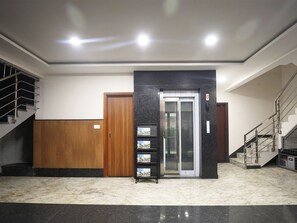 A lobby with a marble floor, a wooden door, a glass elevator, and a staircase with metal railings. - Legacy Square (Bengaluru)