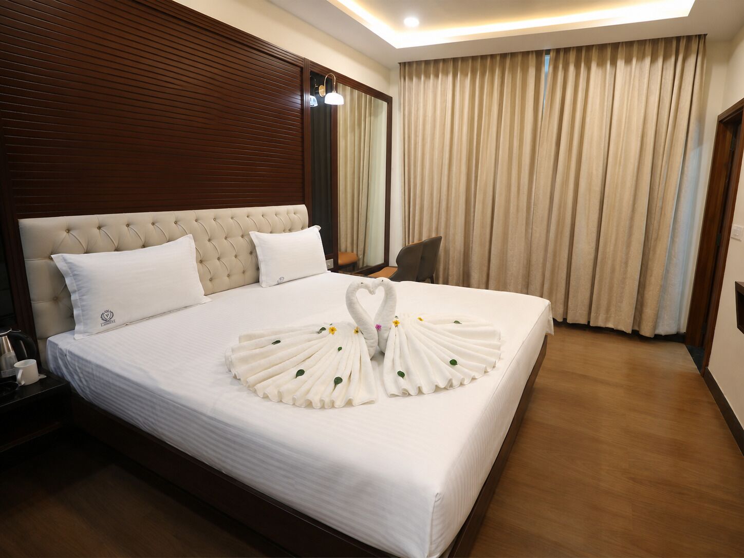 A hotel room with a large bed, a wooden headboard, a bedside table with a lamp, and a chair.