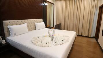 A hotel room with a large bed, a wooden headboard, a bedside table with a lamp, and a chair.