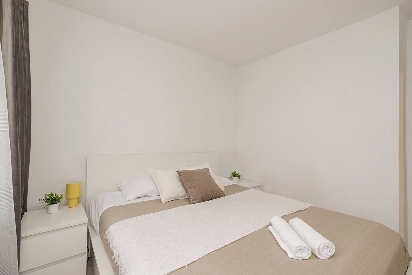 Habitación de hotel con cama, mesita de noche, lámpara y una pequeña planta.