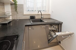 A modern kitchen with a built-in dishwasher, a sink, and a window with sheer curtains. - Bonifraterska Apartment (Warszawa)