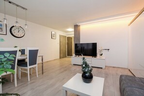 A modern living room with a flat-screen TV, a dining area with chairs, a small Christmas tree, and a clock on the wall. - Bonifraterska Apartment (Warszawa)