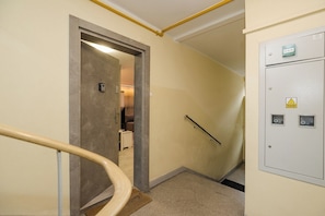 A hallway with a handrail, a door leading to a room, and a utility meter on the wall. - Bonifraterska Apartment (Warszawa)