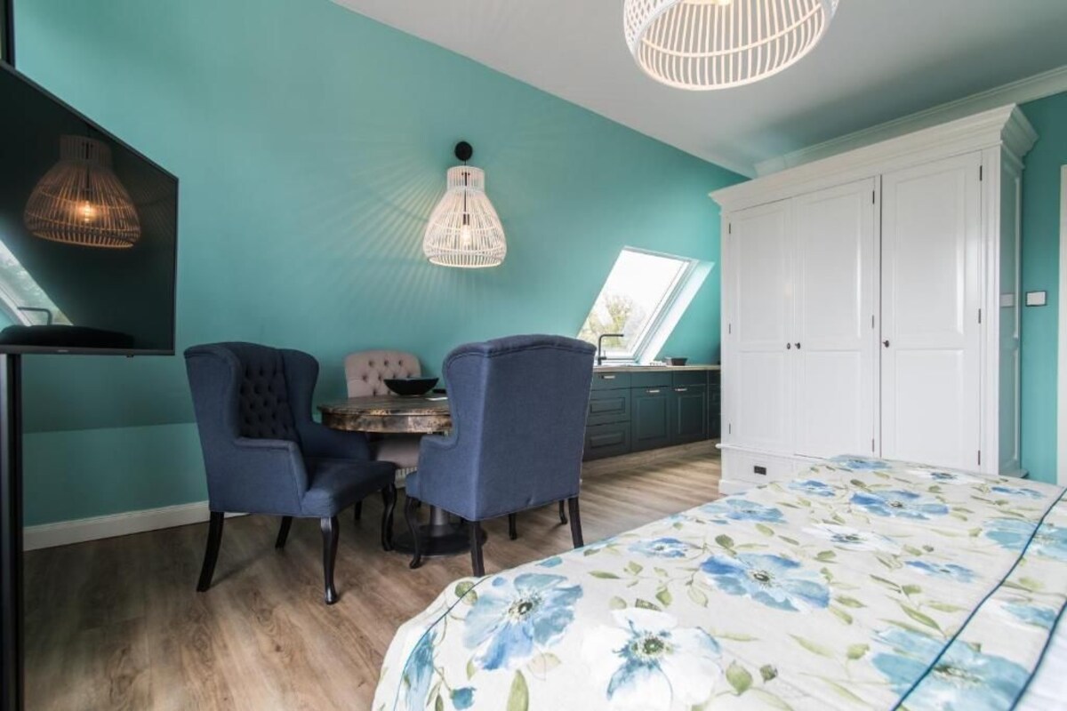 A bedroom with a bed, two chairs, a table, and a wardrobe.