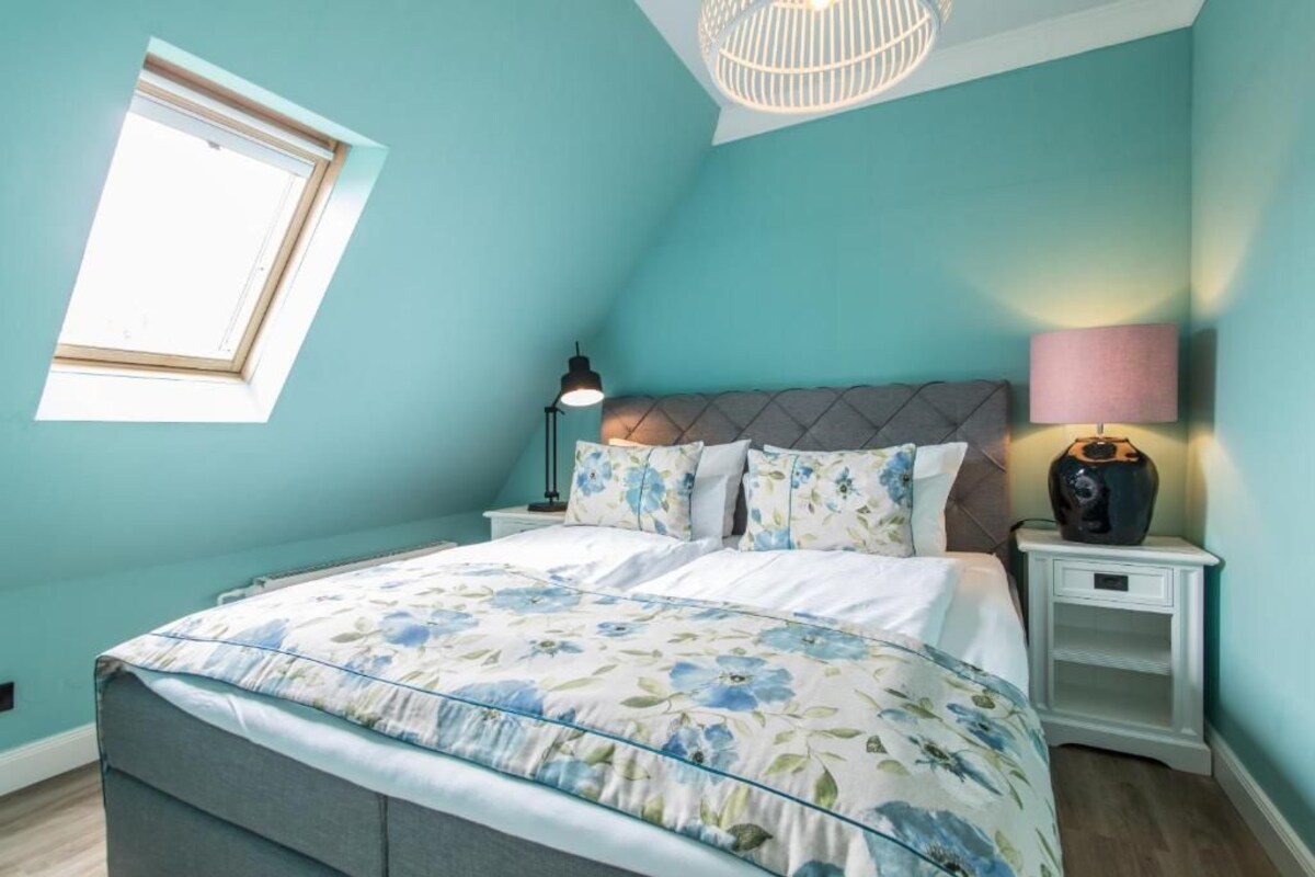 A bedroom with a bed, a nightstand, a lamp, a window, and a ceiling light fixture.