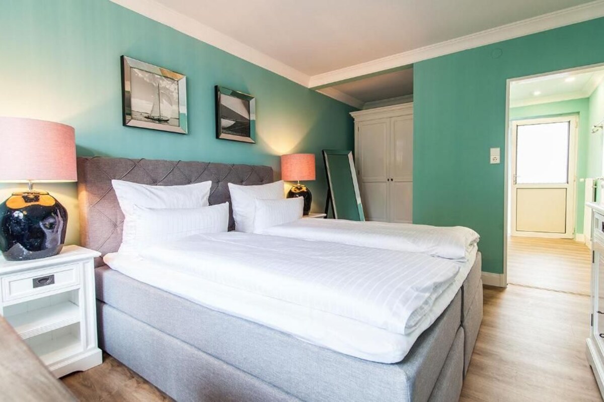 A bedroom with a bed, nightstands, a wardrobe, and a door leading to another room.