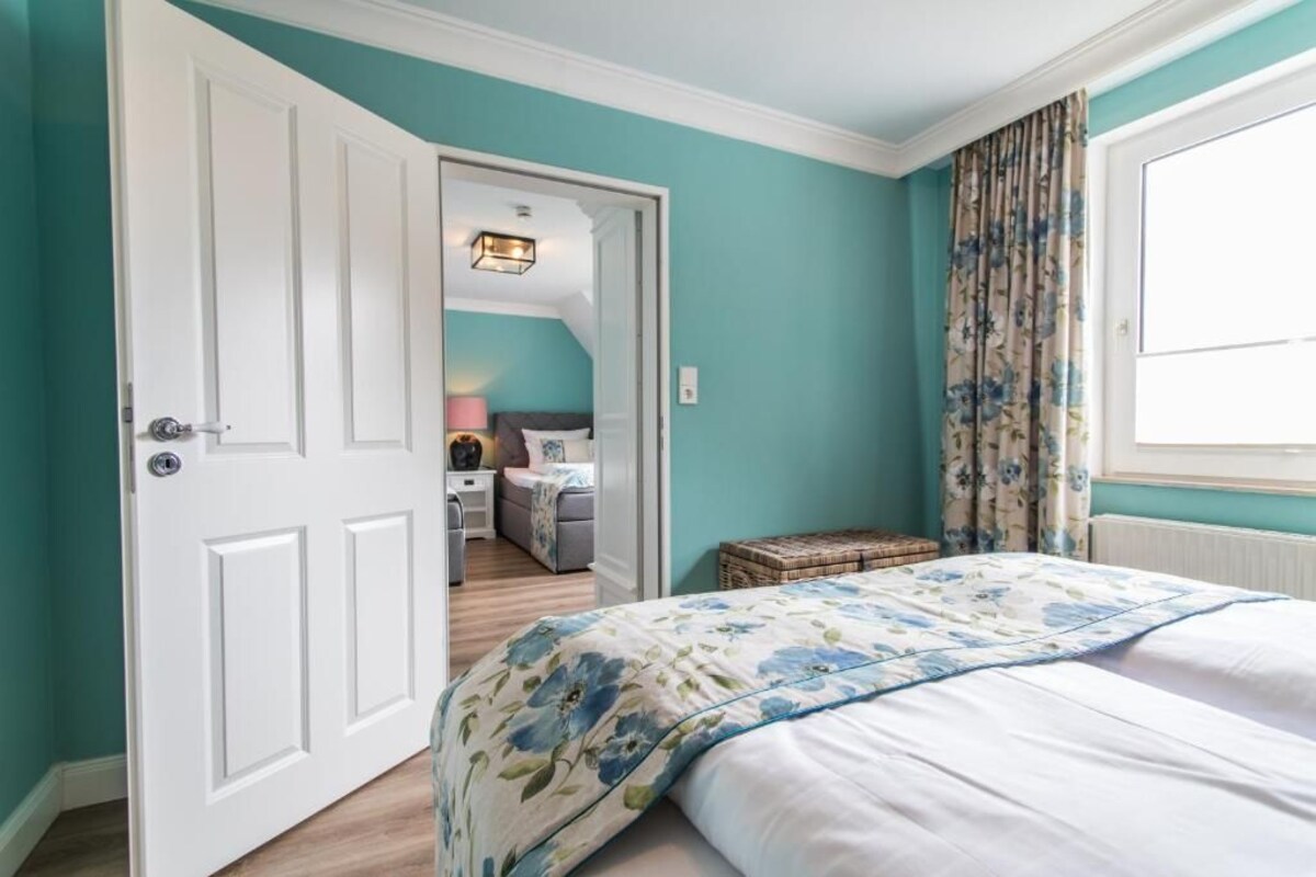 A bedroom with a bed, a door leading to another room, and a window with curtains.