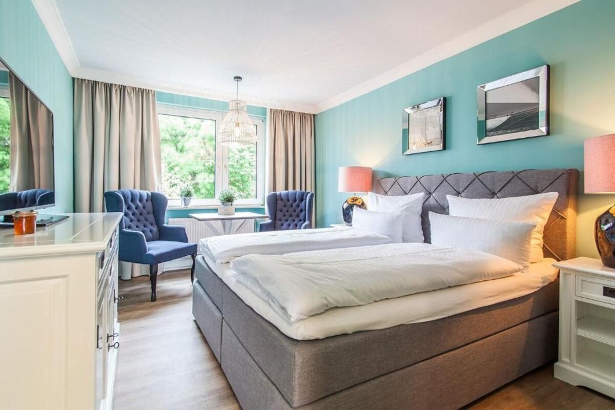 A hotel room with a bed, two armchairs, a desk, and a window with curtains.