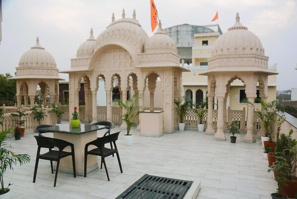 A terrace with a table and chairs, surrounded by potted plants and a building with domed structures.
